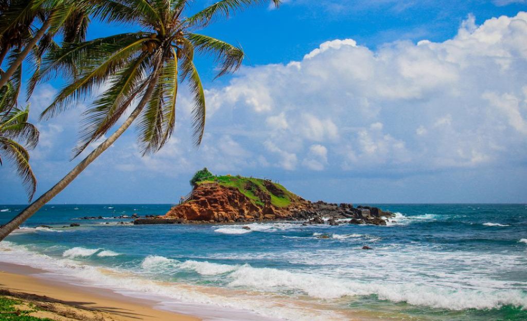 Rocky outcrop offshore with palms and breaking waves on the Mirissa coast